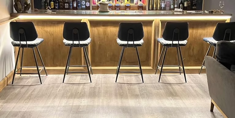 A timber bar counter with a warm LED strip under the lip, lighting the floor and bar stools
